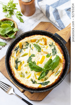Spinach and cheese omelette. Frittata made of eggs, paprika and spinach in a frying pan on a marble countertop. Spinach and cheese omelette. Frittata made of eggs, paprika and spinach in a frying pan on a marble countertop. 92765854