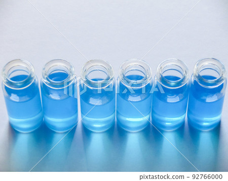 白色建築紙上並排放置的六個裝有藍色液體的玻璃瓶 92766000
