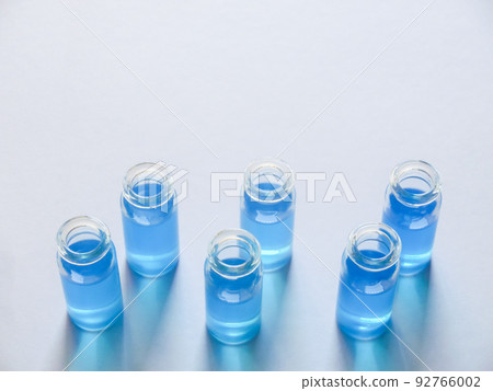 Six glass bottles with blue liquid arranged on white construction paper Six glass bottles with blue liquid arranged on white construction paper 92766002