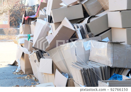 Cardboard and waste paper is collected and packaged for recycling in city in sunny day. Pile of cardboard is sorting for recycled. 92766150