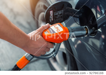Close-up detail view of fuel autogas pump gun connected with noozle adapter to car tank to refill at car gas filling station. Refueling vehicle with liquefied lpg or lng product. Safety technology Close-up detail view of fuel autogas pump gun connected with noozle adapter to car tank to refill at car gas filling station. Refueling vehicle with liquefied lpg or lng product. Safety technology 92766188