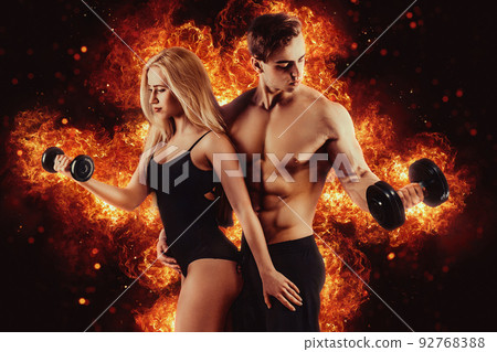 Muscular couple body in studio. Couple of fit bodybuilders, muscular man and beautiful sexy girl with dumbbells. Sport couple. Fire background Muscular couple body in studio. Couple of fit bodybuilders, muscular man and beautiful sexy girl with dumbbells. Sport couple. Fire background 92768388