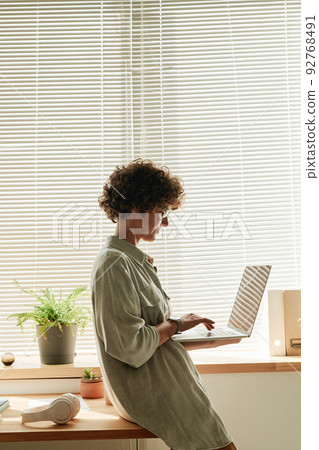Young businesswoman leaning on her office desk and typing on laptop, she communicating online 92768491
