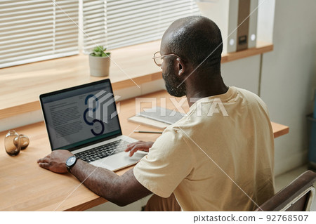 Rear view of African young businessman sitting at his workplace with laptop and typing document online 92768507
