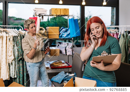 female coworkers, working in the warehouse of the clothing shop, receiving calls from their customers and provider. mature businesswoman and young employee. business concept and entrepreneur. 92768885