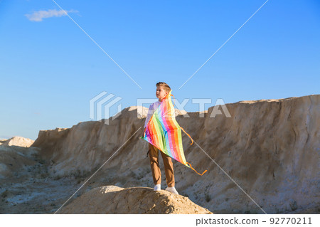A boy with a kite stands on a mountain and looks into the distance. The concept of freedom and fantasy 92770211