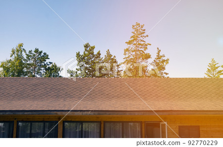 The roof of a wooden house is covered with flexible tiles in the rays of sunlight. Close-up The roof of a wooden house is covered with flexible tiles in the rays of sunlight. Close-up 92770229