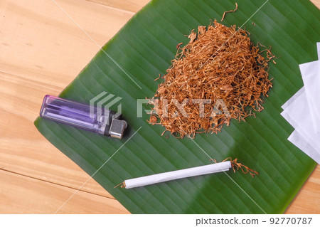 Homemade dry tobacco and cigarette over banana leave on the brown wooden table. Homemade dry tobacco and cigarette over banana leave on the brown wooden table. 92770787