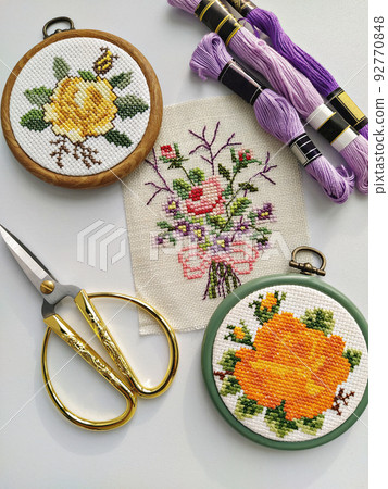Vintage wooden embroidery hoops, scissors, needle, thread and fabric with floral cross-stitch embroidery on white, top view 92770848
