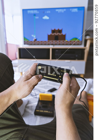Male hands holding joystick from video-game console against background of home interior and TV-screen. First-person view. Home entertainment concept Male hands holding joystick from video-game console against background of home interior and TV-screen. First-person view. Home entertainment concept 92770859