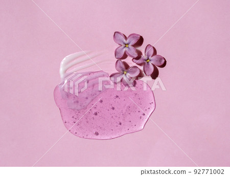 Texture of white cream and pink gel drop with lilac flower on pink background. Smear of moisturizer closeup. Lotion swatch. Beauty, skin care product smear smudge drop. SPF sunscreen cream sample 92771002