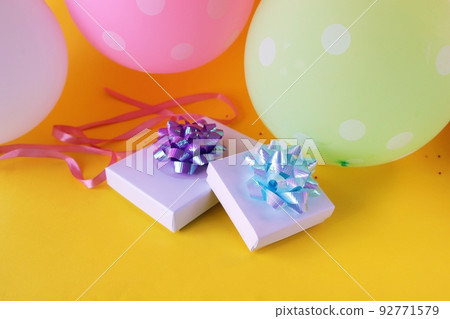Gift boxes decorated with a bow of shiny ribbon, holiday balloons, bright yellow background, concept of congratulations, surprise, happy birthday 92771579