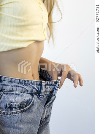 A girl in oversized jeans on a white background. Weight loss and diet. 92771751