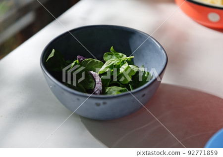 Close-up of freshly picked basil leaves - fragrant culinary herbs in a navy blue ceramic bowl on white table background Close-up of freshly picked basil leaves - fragrant culinary herbs in a navy blue ceramic bowl on white table background 92771859