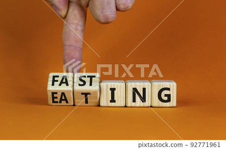 Fasting or eating symbol. Doctor turns wooden cubes and changes the word 'eating' to 'fasting'. Beautiful orange background, copy space. Healthy eating, medical and time to fasting concept. Fasting or eating symbol. Doctor turns wooden cubes and changes the word 'eating' to 'fasting'. Beautiful orange background, copy space. Healthy eating, medical and time to fasting concept. 92771961