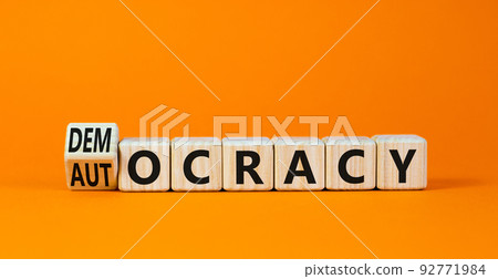 Democracy or autocracy symbol. Turned wooden cubes and changed the concept word Autocracy to Democracy. Beautiful orange background. Copy space. Business democracy or autocracy concept. 92771984