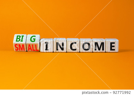Big or small income symbol. Turned wooden cubes and changed concept words Small income to Big income. Beautiful orange table orange background, copy space. Business big or small income concept. 92771992