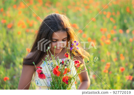 Beautiful girl in the poppy field. Holding beautiful flowers. summer time. Young girl smells flowers in the field 92772019