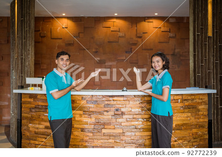 two employees wearing uniforms smiling with hand gestures presenting something 92772239