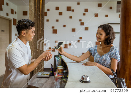 Female guest showing smartphone at receptionist for proof of booking 92772299