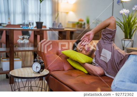 Young Asian man sleeping in bed with clock 92772302