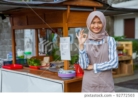 woman standing in front of her small traditional food shop and showing thumb up woman standing in front of her small traditional food shop and showing thumb up 92772503
