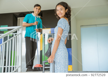 Smiling female guest going up stairs carrying bags and suitcases 92772520
