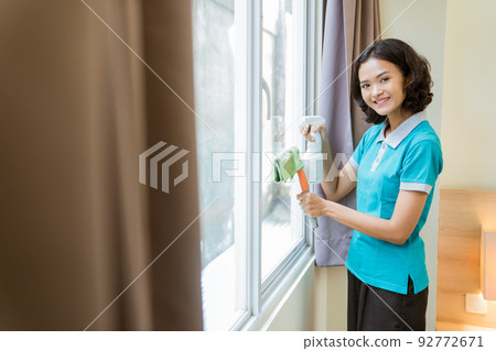 smiling female housekeeper in turquoise uniform wiping windows smiling female housekeeper in turquoise uniform wiping windows 92772671