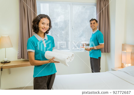 Smiling female housekeeper in turquoise uniform holding towel standing Smiling female housekeeper in turquoise uniform holding towel standing 92772687