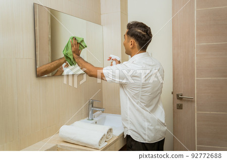 Male janitor spraying and wiping the mirror with rag Male janitor spraying and wiping the mirror with rag 92772688