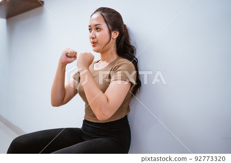 asian woman squating against the wall at home 92773320