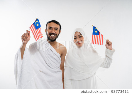 Smiling asian couple wearing ihram clothes carrying small Malaysian flag Smiling asian couple wearing ihram clothes carrying small Malaysian flag 92773411