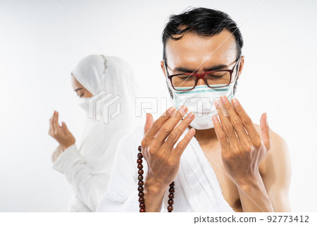 Man wearing ihram clothes and mask performing al fatihah prayer Man wearing ihram clothes and mask performing al fatihah prayer 92773412