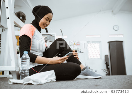 beautiful muslim sporty woman taking a break after exercising using phone 92773413