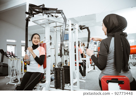 woman using chest press machine at the gym with friend woman using chest press machine at the gym with friend 92773448