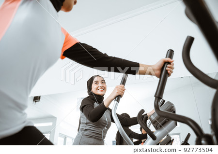 woman with hijab exercising with friend on static elliptical cycle machine woman with hijab exercising with friend on static elliptical cycle machine 92773504