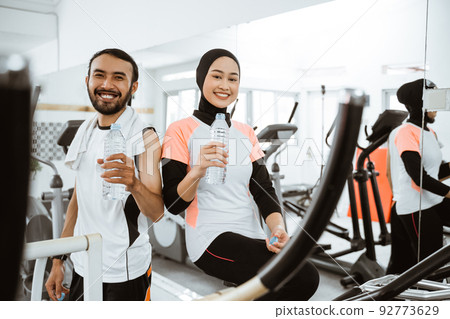muslim couple having a bottle of water while exercising at the gym muslim couple having a bottle of water while exercising at the gym 92773629