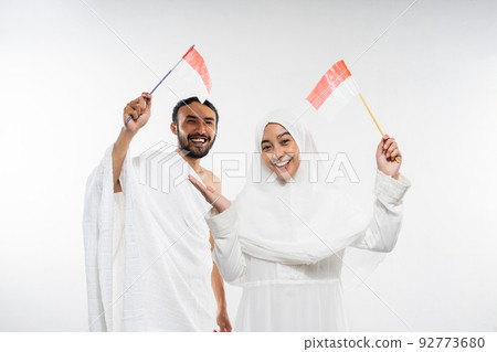 Excited couple of prospective Hajj pilgrims carrying Indonesian flags standing 92773680