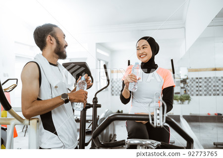 muslim couple having fun at the gym while enjoying a bottle of water together muslim couple having fun at the gym while enjoying a bottle of water together 92773765