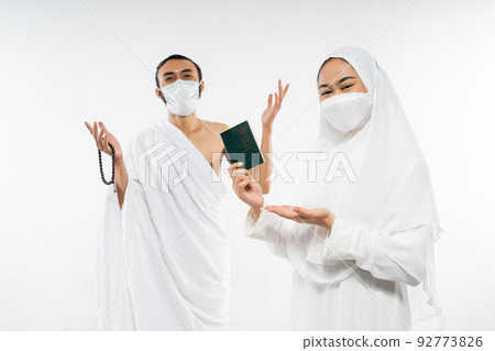 Happy asian couple wearing ihram clothes holding a passport Happy asian couple wearing ihram clothes holding a passport 92773826