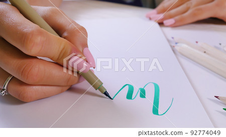 Calligrapher hands writes word on white paper. Inscribing ornamental decorated letters. Calligraphy Calligrapher hands writes word on white paper. Inscribing ornamental decorated letters. Calligraphy 92774049