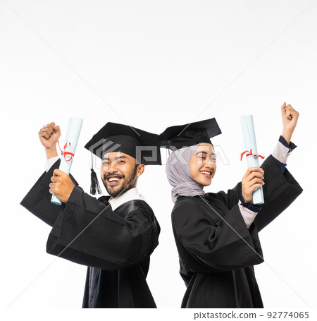 Confident graduates wearing togas holding certificate while celebrating standing 92774065