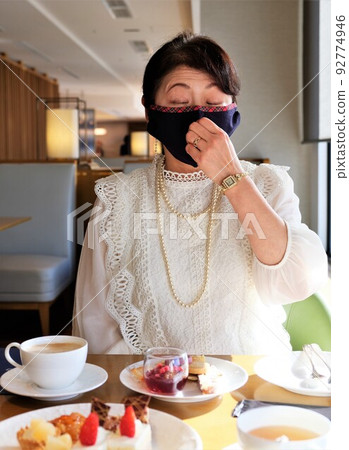 A woman wearing a mask attending tea time in a hotel lounge 92774946