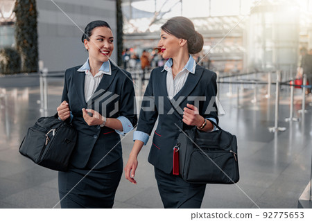 Smiling pretty flight attendants with bags talking in the terminal 92775653