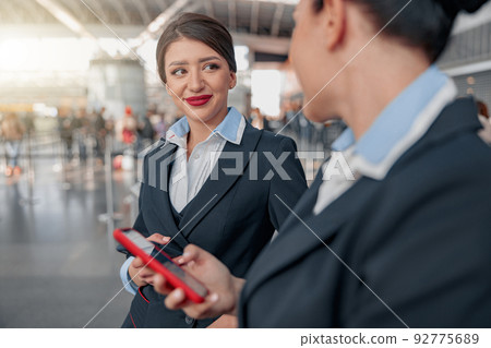 Two beautiful stewardesses using phones and talking in the airport Two beautiful stewardesses using phones and talking in the airport 92775689