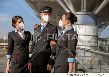 Pilot and two stewardesses wearing face masks and standing outdoor 92775746