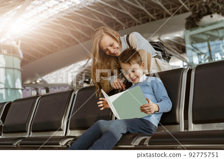 Mom and son in the airport lounge watching something on digital tablet before the flight Mom and son in the airport lounge watching something on digital tablet before the flight 92775751