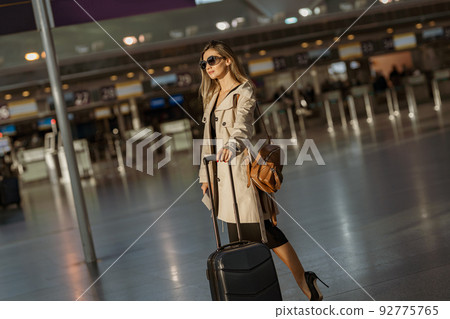 Young woman traveler in sunglasses with luggage waiting check in in airport before boarding Young woman traveler in sunglasses with luggage waiting check in in airport before boarding 92775765