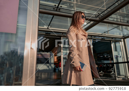 Young lady in trench coat with a suitcase leaving the airport terminal 92775918