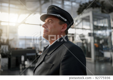 Smiling pilot standing and looking at airport terminal 92775936